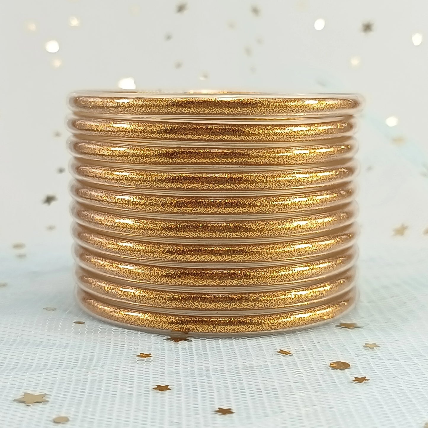 Set de 10 pulseras de silicona con glitter, en tonos cálidos dorados, ideales para complementar cualquier look femenino.