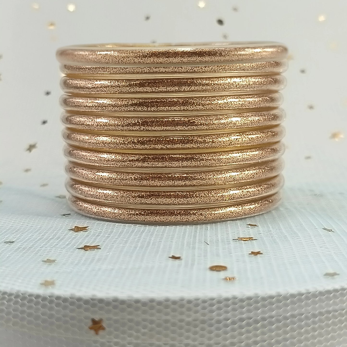 Set de 10 pulseras de silicona con glitter, en tonos cálidos dorados, ideales para complementar cualquier look femenino.