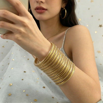 Set de 10 pulseras de silicona con glitter, en tonos cálidos dorados, ideales para complementar cualquier look femenino.